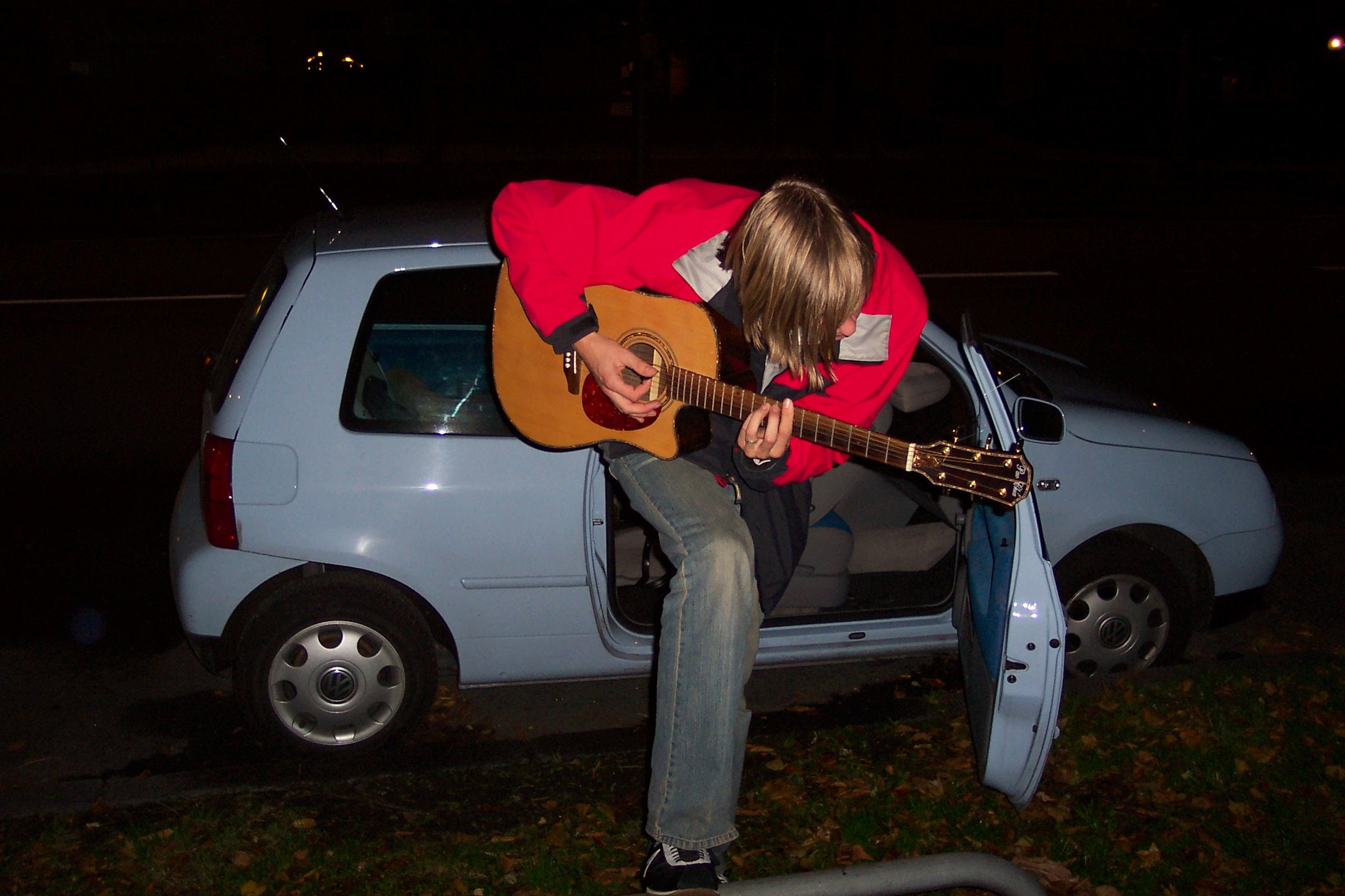 Johannes "JoJo" Kinder steht mit akustischer Gitarre vor seibnme blauen VW Lupo und singt
